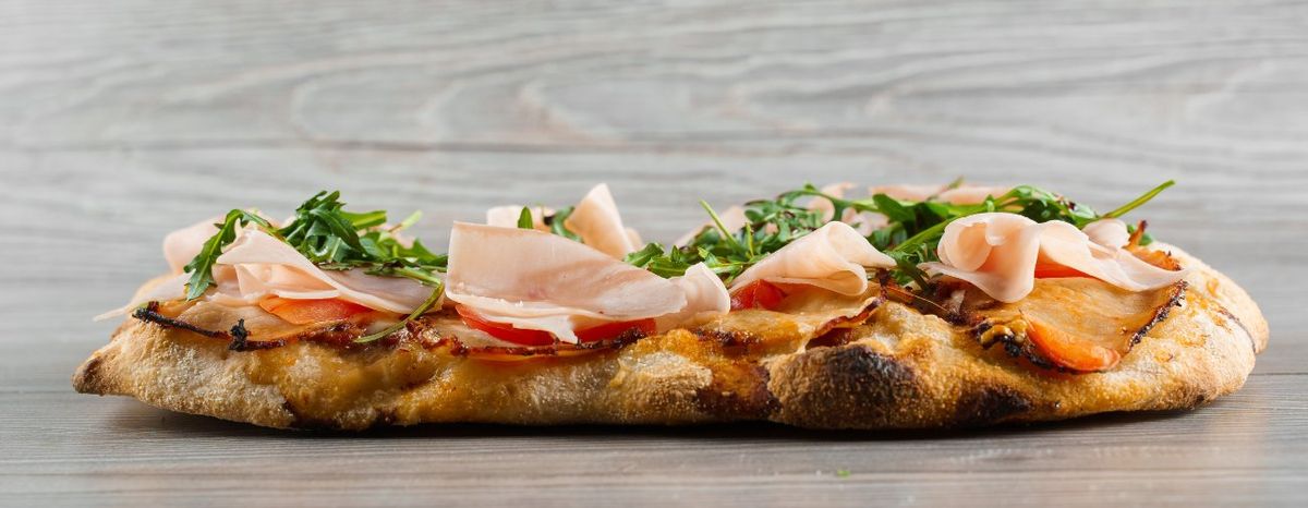 Una pinsa romana con prosciutto cotto, rucola e pomodorini